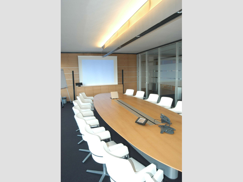ovaler Konferenztisch mit weißen Stühlen und Beamer, Ansicht auf die Leinwand